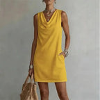 Front view of a sleeveless yellow mini dress with a soft cowl neckline, shown with a woven tote bag