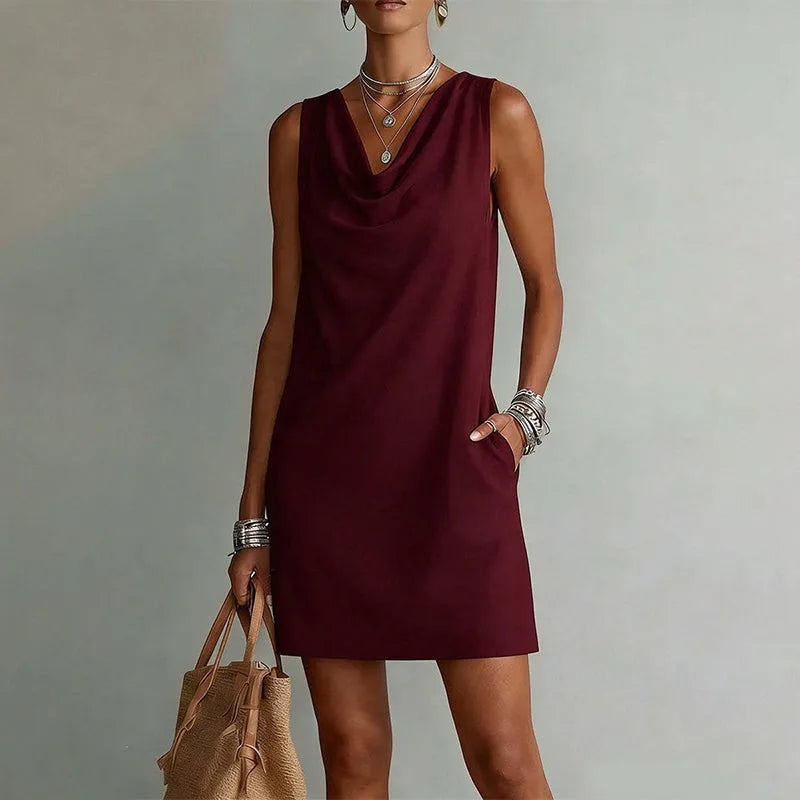 Close-up of the cowl neckline drape on a sleeveless mini dress, paired with layered silver jewellery