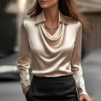 Close-up of beige satin blouse with draped cowl neckline, collar and layered necklace worn over a black skirt