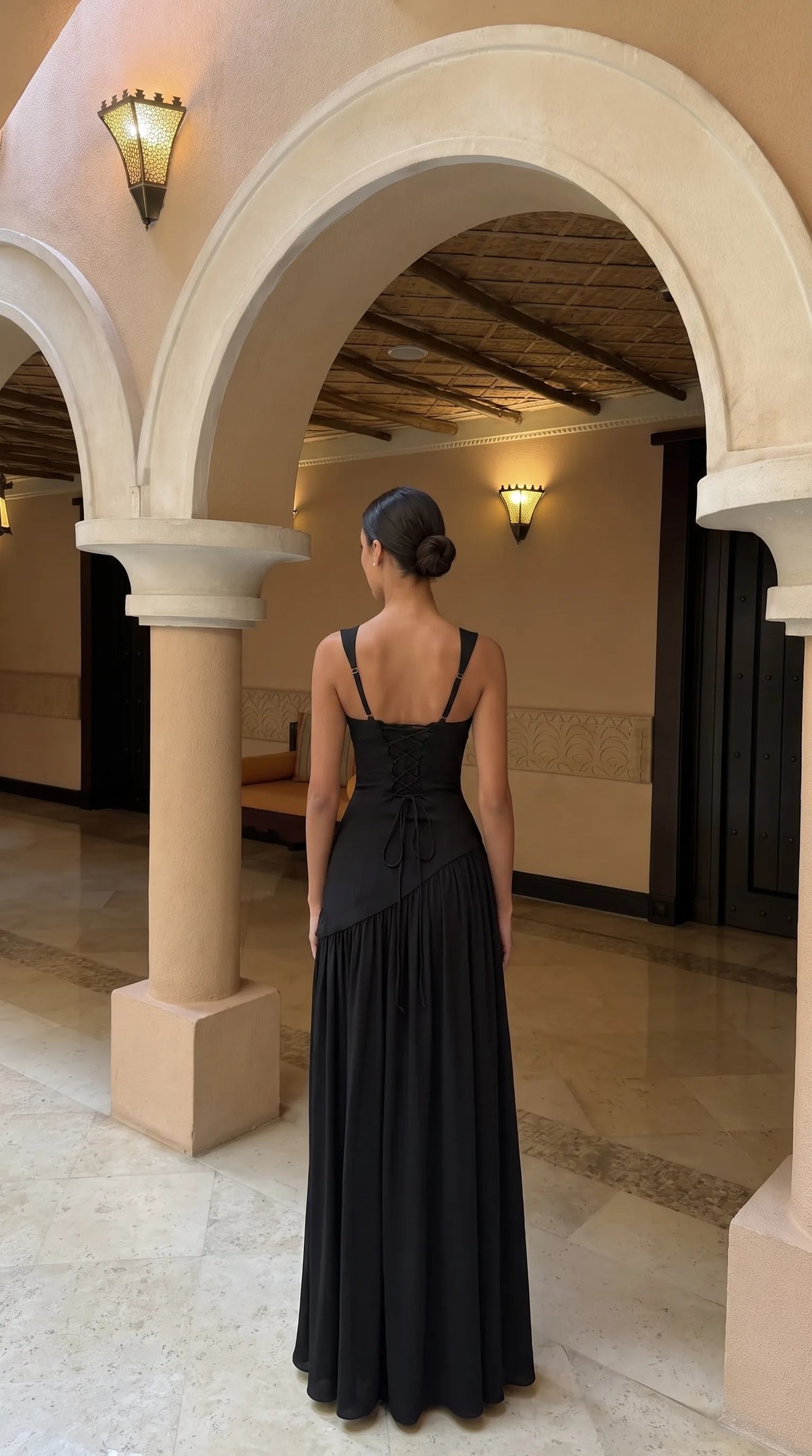 Back view of black maxi dress showing lace-up corset back detail, adjustable straps and flowing pleated skirt
