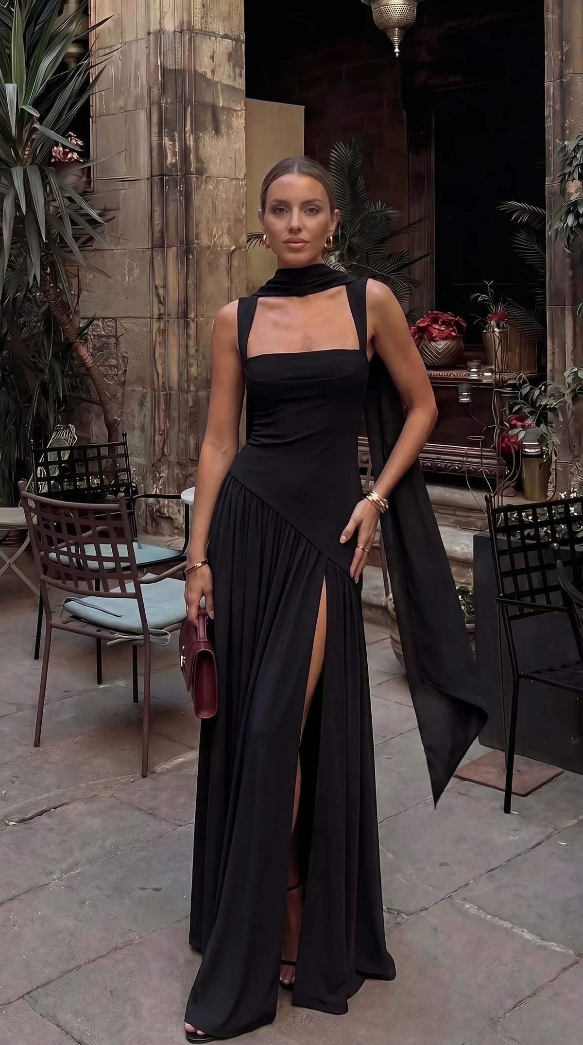 Close-up front view of black square-neck maxi dress with draped neck scarf, thigh split and gold bracelets