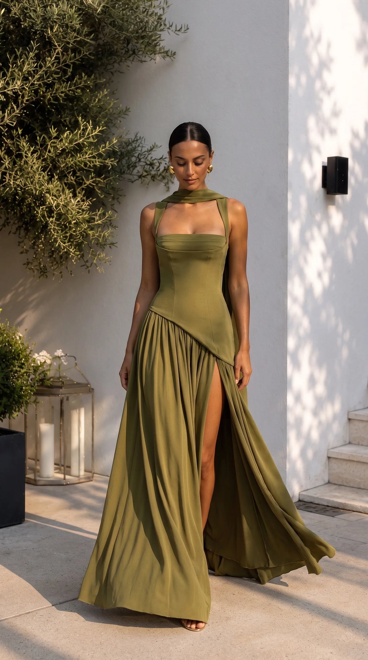 Front view of olive green maxi dress with structured bodice, draped scarf and thigh split flowing in the breeze