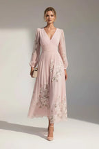 Model wears a blush pink floral chiffon midi dress with long sheer sleeves and a draped V-neckline, standing in natural light