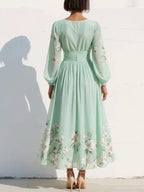 Back view of the sage green floral dress revealing the gathered waist detail and the sweep of the pleated midi skirt