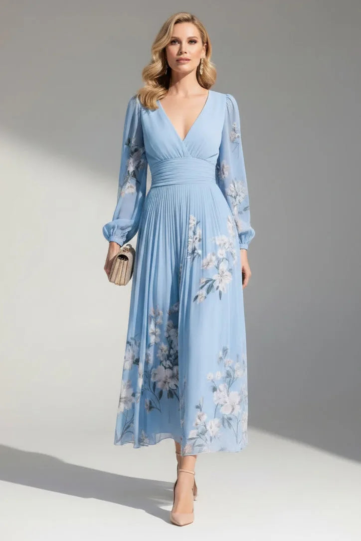 Model wears the dress in dusty blue, showing the full-length silhouette with sheer floral sleeves and pleated skirt