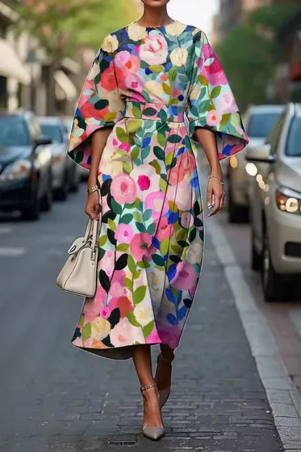 Model wears a floral print kimono-sleeve midi dress in pink, cream and green with a white handbag and nude heels