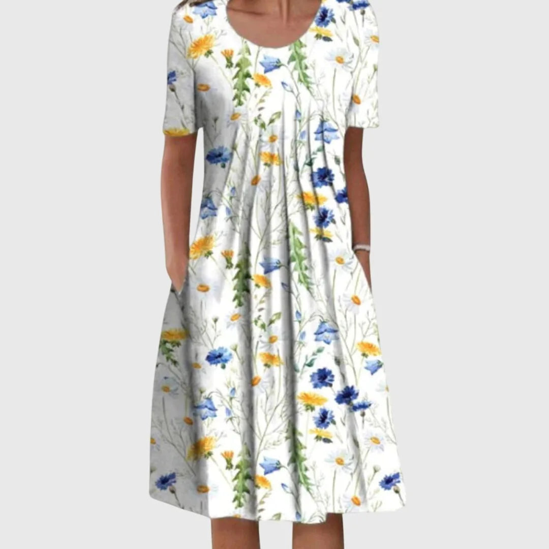 Close-up front view of a white floral midi dress with yellow dandelions, blue cornflowers and daisies, round neckline and pleated bodice