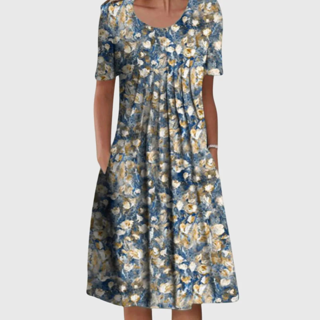 Front view of a blue and gold floral midi dress with a painterly print, round neckline, pleated front and hand pockets