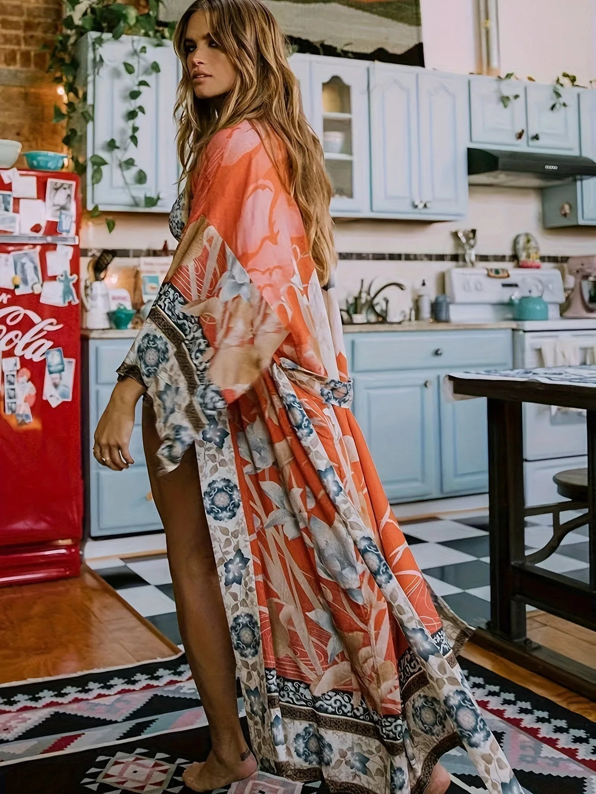 Model in rust orange floral print kimono flowing open over a slip, walking through a boho kitchen
