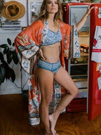 Model wearing rust orange kimono open over a blue printed bikini beside a vintage red fridge