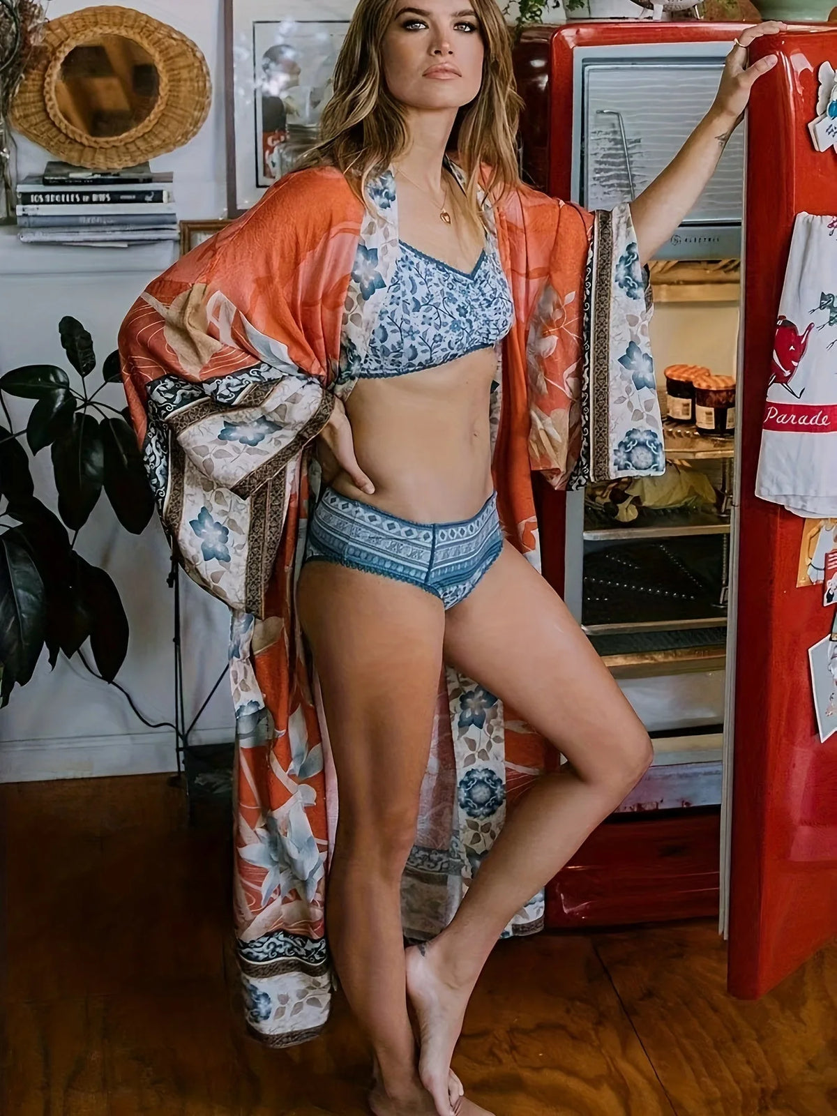 Model wearing rust orange kimono open over a blue printed bikini beside a vintage red fridge