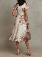 Back view of the ivory floral satin midi dress showing the flared skirt, fitted bodice seam and flutter sleeve detail