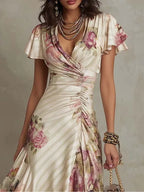 Close-up of the wrap V-neckline, ruched bodice and blush rose print on the satin midi dress, paired with layered necklaces