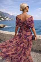 Close-up of the off-shoulder neckline and twist detail on the purple floral chiffon dress paired with a beaded clutch