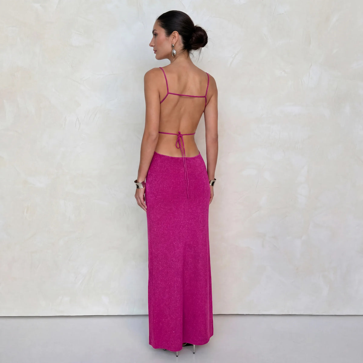Back view against a plain backdrop showing the open back, thin tie straps and rib-knit skirt of the pink dress