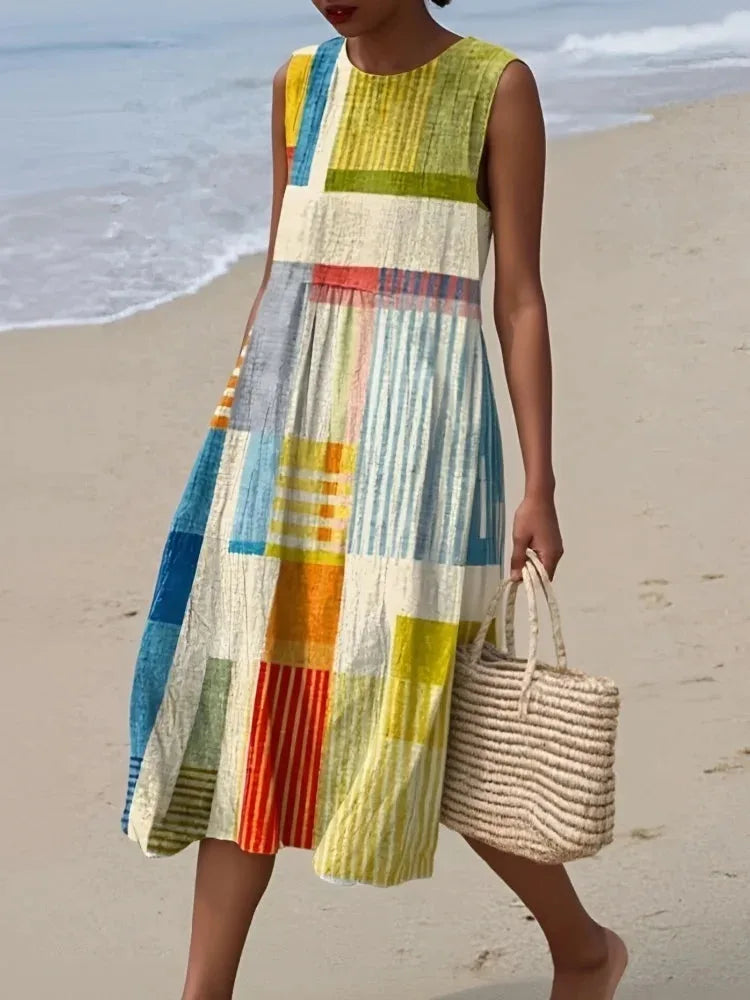 Woman walking on a sandy beach wearing a sleeveless colour-block midi dress in yellow, blue and cream geometric patchwork print.