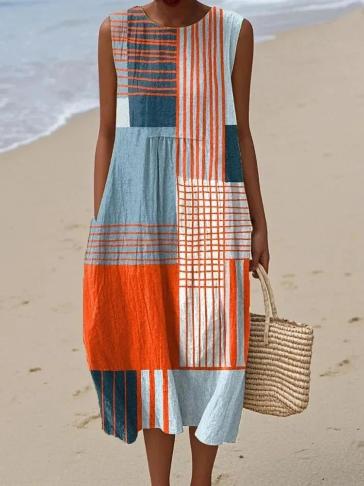 Sleeveless midi dress in bold orange and navy geometric patchwork print with fine stripe detailing, styled with a straw tote bag.