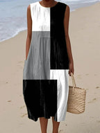 Sleeveless midi dress in black, white and grey colour-block geometric print, worn on sand near the water's edge.