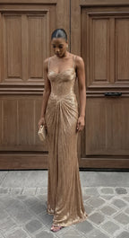 Front view of model in gold shimmer corset-bodice maxi dress with draped skirt against carved wooden doors
