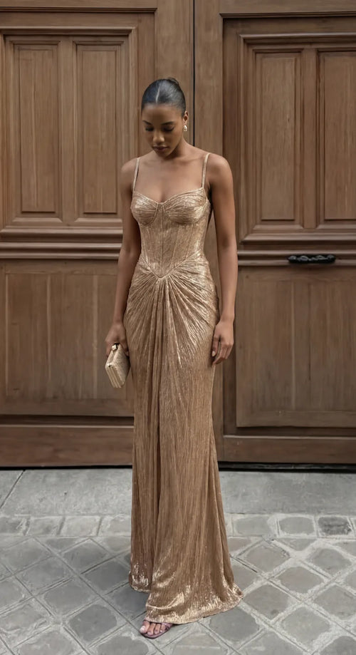 Front view of model in gold shimmer corset-bodice maxi dress with draped skirt against carved wooden doors