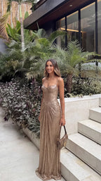 Side angle of gold metallic maxi dress showing fitted corset bodice and flowing pleated fabric near steps