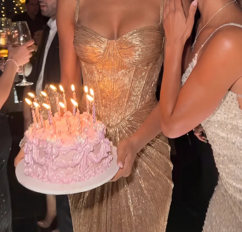Close-up of gold corset bodice texture with boning detail and thin straps, model holding a birthday cake