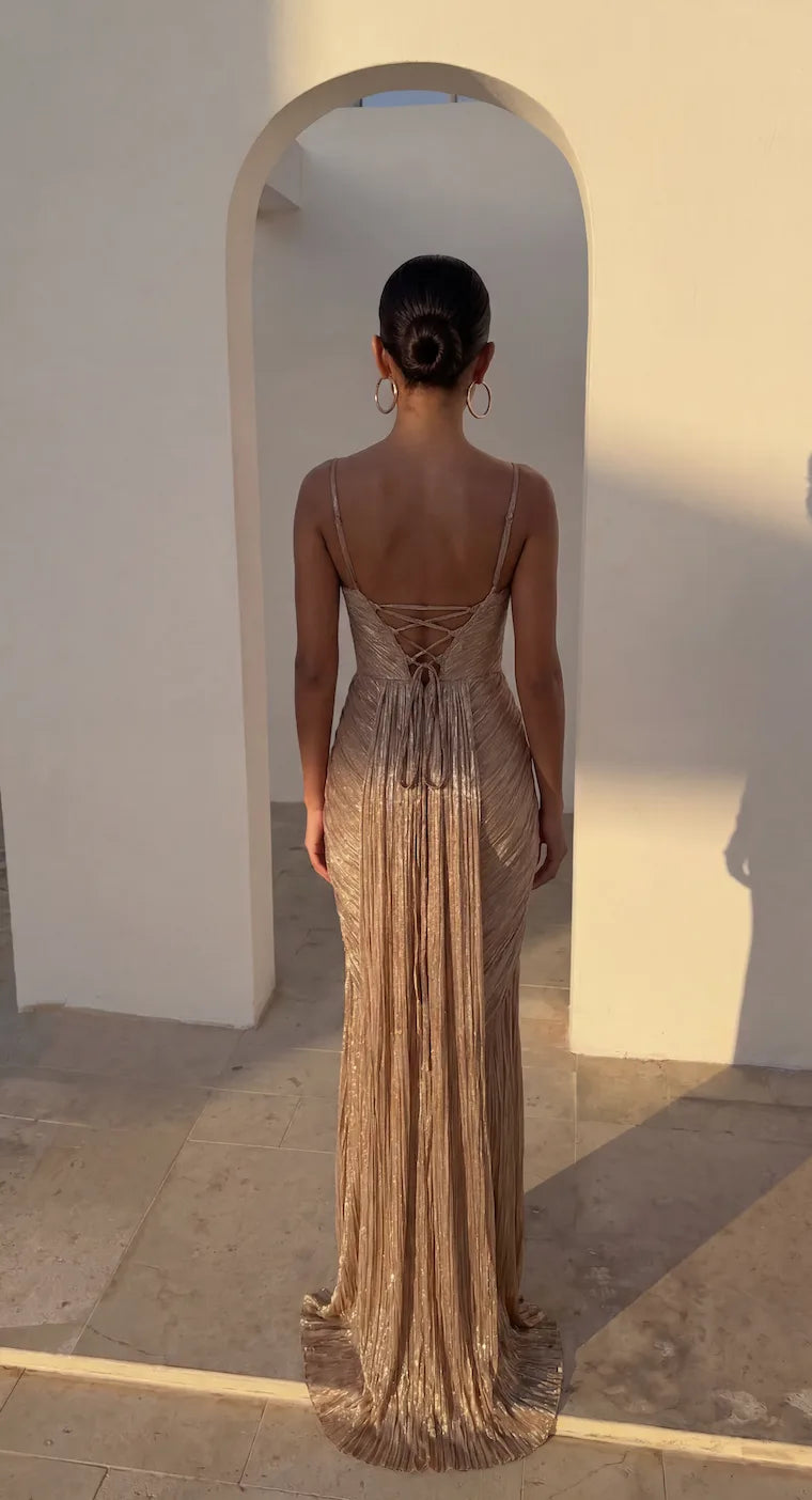 Back view showing lace-up corset detailing and open back of the gold pleated maxi dress in sunlight