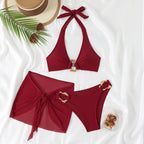 Flat lay of the burgundy two-piece bikini with mesh wrap sarong, styled with a straw hat, sunglasses and palm leaf