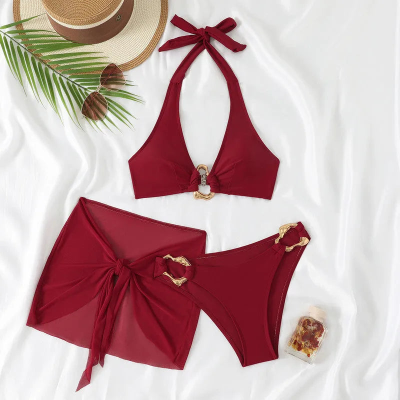 Flat lay of the burgundy two-piece bikini with mesh wrap sarong, styled with a straw hat, sunglasses and palm leaf