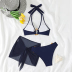 Flat lay of navy halter bikini top and high-leg bottoms with gold rings, shown with a round straw hat and tulips