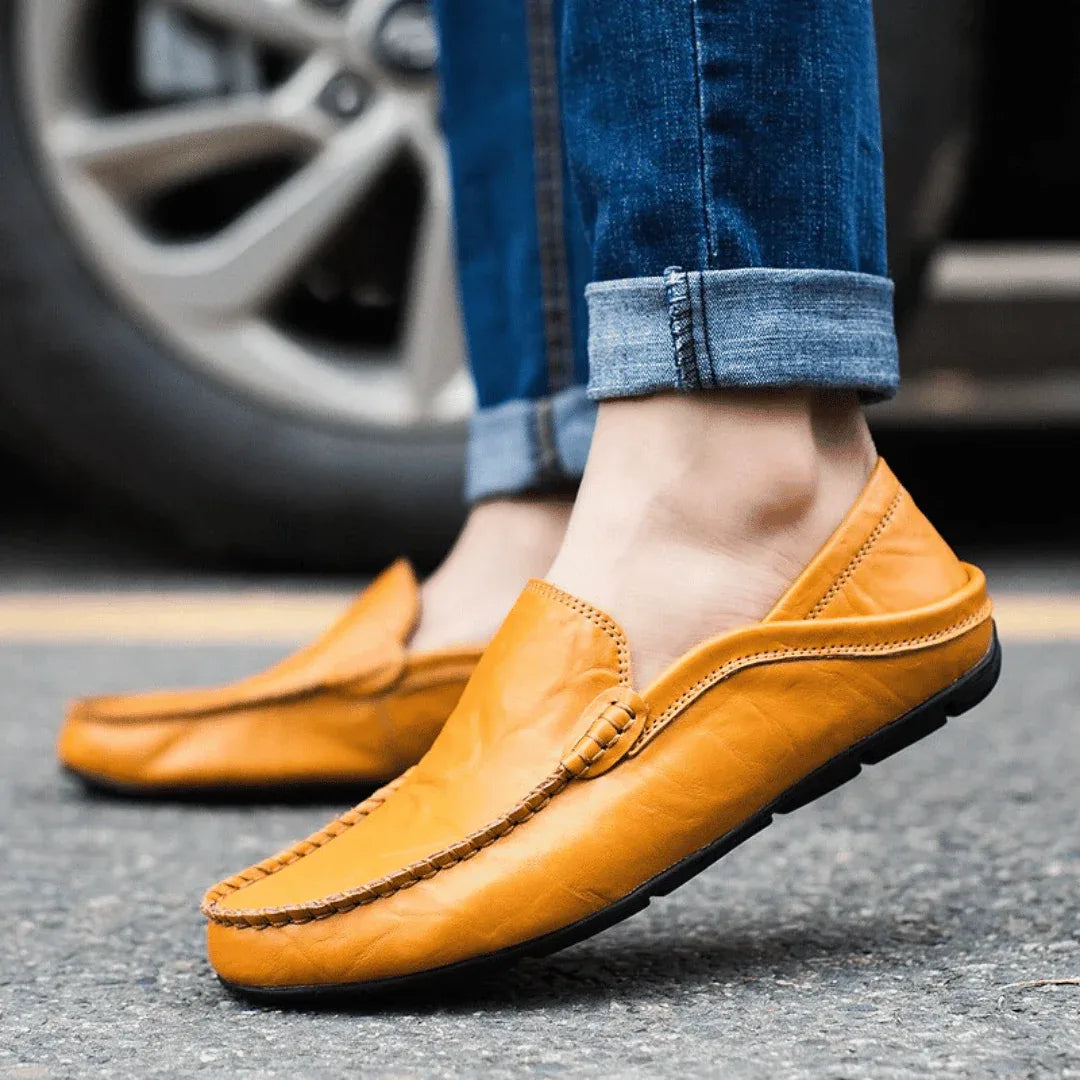 Close-up side view of tan leather loafer worn with cuffed denim jeans, standing beside a car wheel