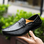 Black leather loafer held up by hand, revealing the tan interior lining and stitched vamp