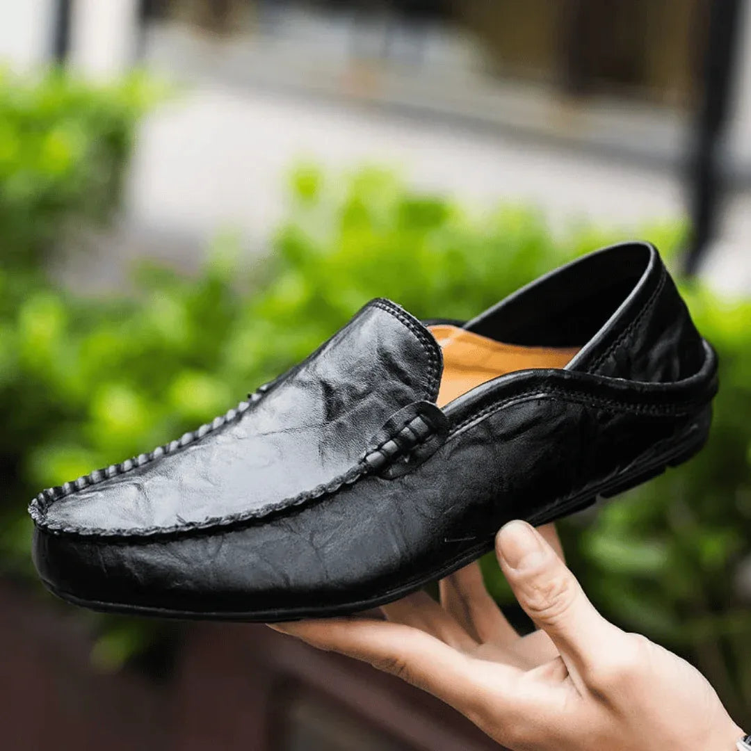 Black leather loafer held up by hand, revealing the tan interior lining and stitched vamp