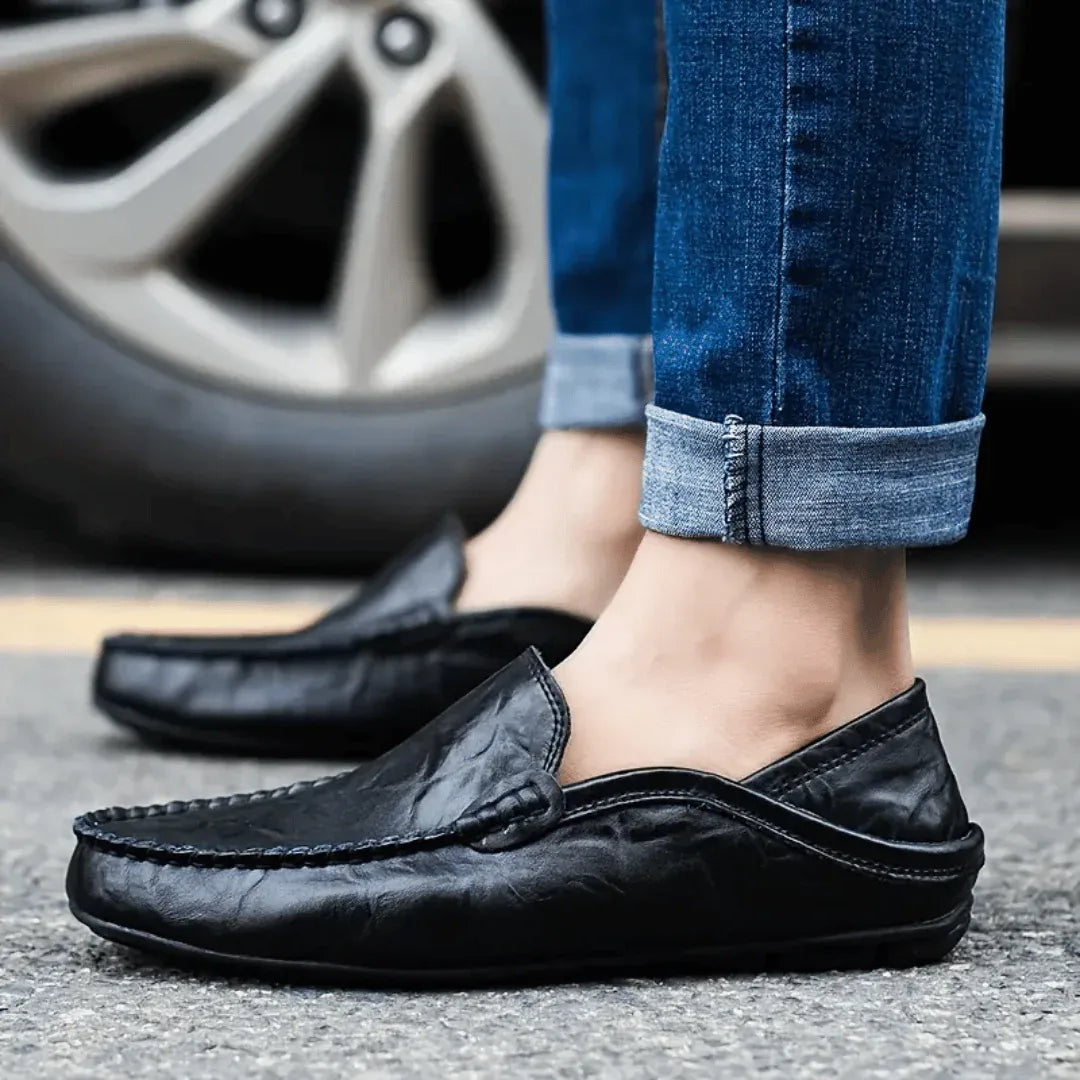 Close-up of black leather loafers worn with cuffed jeans, standing on pavement