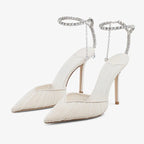 Front angled view of a pair of ivory mesh pointed-toe heels with ruched draping and a crystal ankle strap