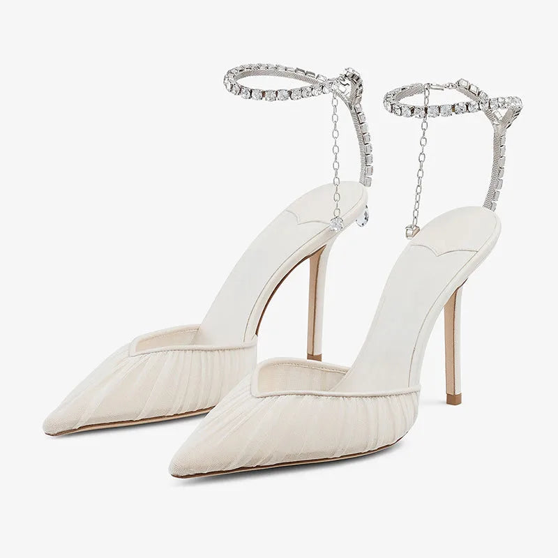 Front angled view of a pair of ivory mesh pointed-toe heels with ruched draping and a crystal ankle strap