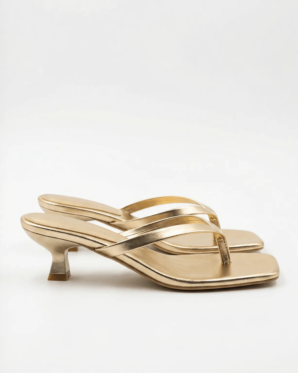 Pair of gold metallic thong sandals with crossover straps and spool-style kitten heel