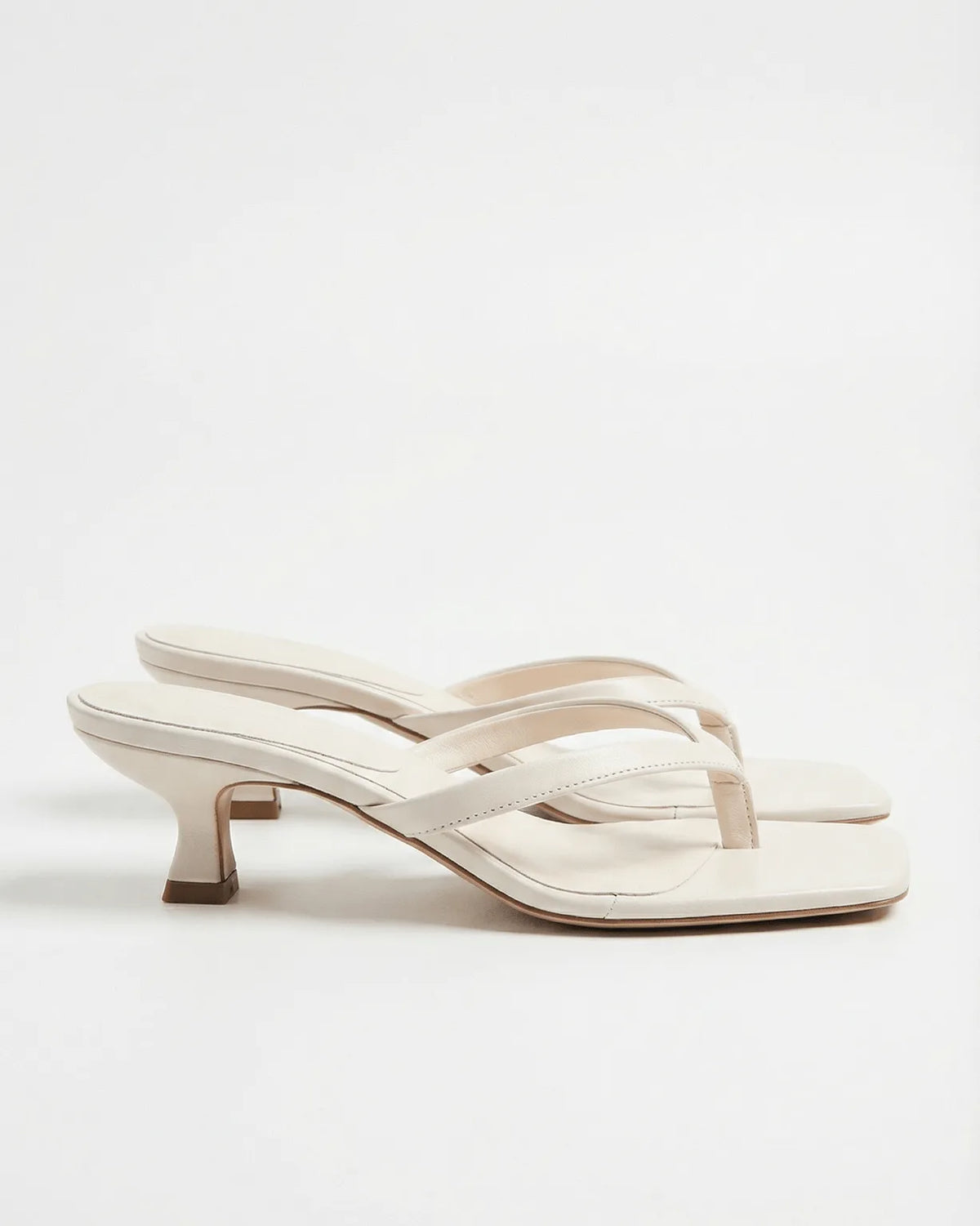 White leather thong sandals showing cutout strap detail and flared kitten heel