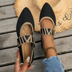 Close-up of black knit pointed-toe flats with gold zebra-pattern strap, modelled on feet beside a straw hat