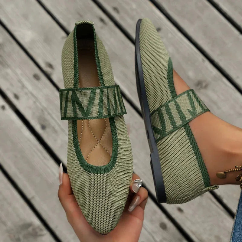 Close-up of black and gold strap detail on knit flats worn on feet with rings and bracelet accessories