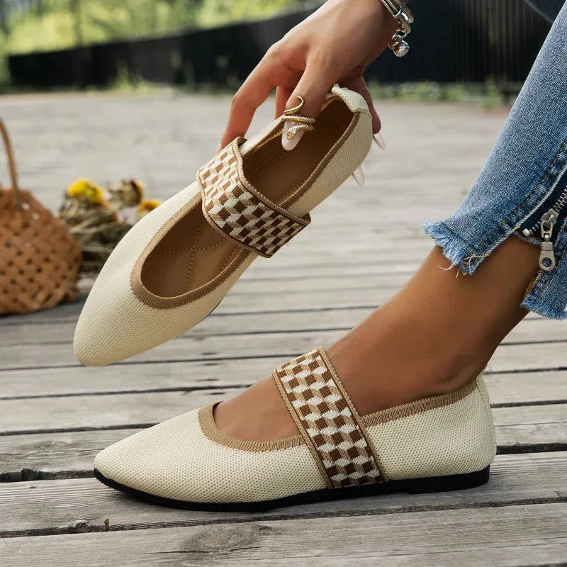 Side view of beige knit flats with checkerboard strap held in hand, worn with denim near a straw tote