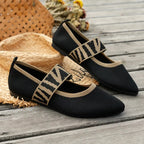 Angled view of black knit flats with tan zebra-print strap resting on timber decking beside a straw bag