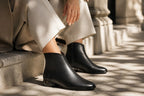 Close-up of black ankle boots with back zip detail worn with white trousers
