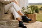 Black leather ankle boots worn with cream jeans on a stone step outdoors