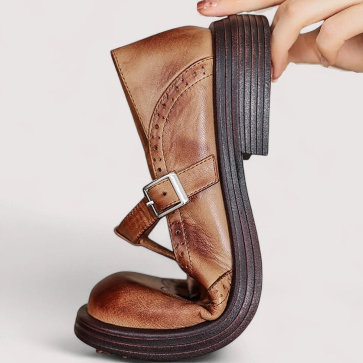 Side profile held by hand, showing the stacked wooden-look heel and brogue perforated edging on tan leather