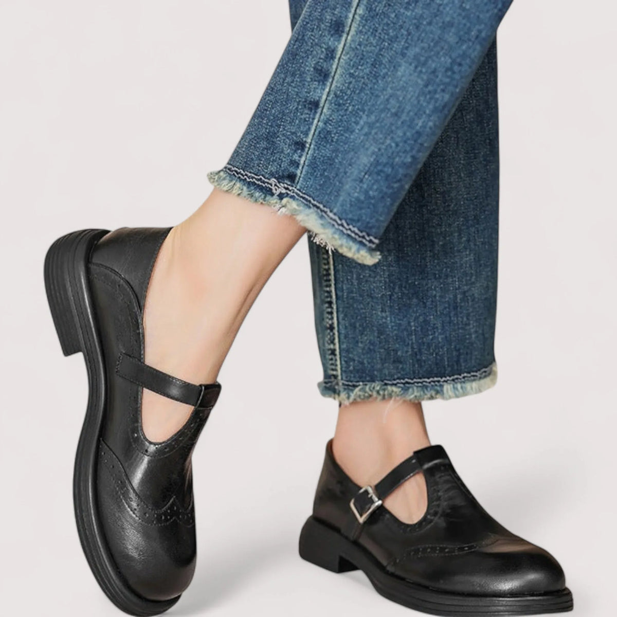 Black leather T-strap Mary Janes worn on foot with cuffed denim jeans, side angle while stepping forward