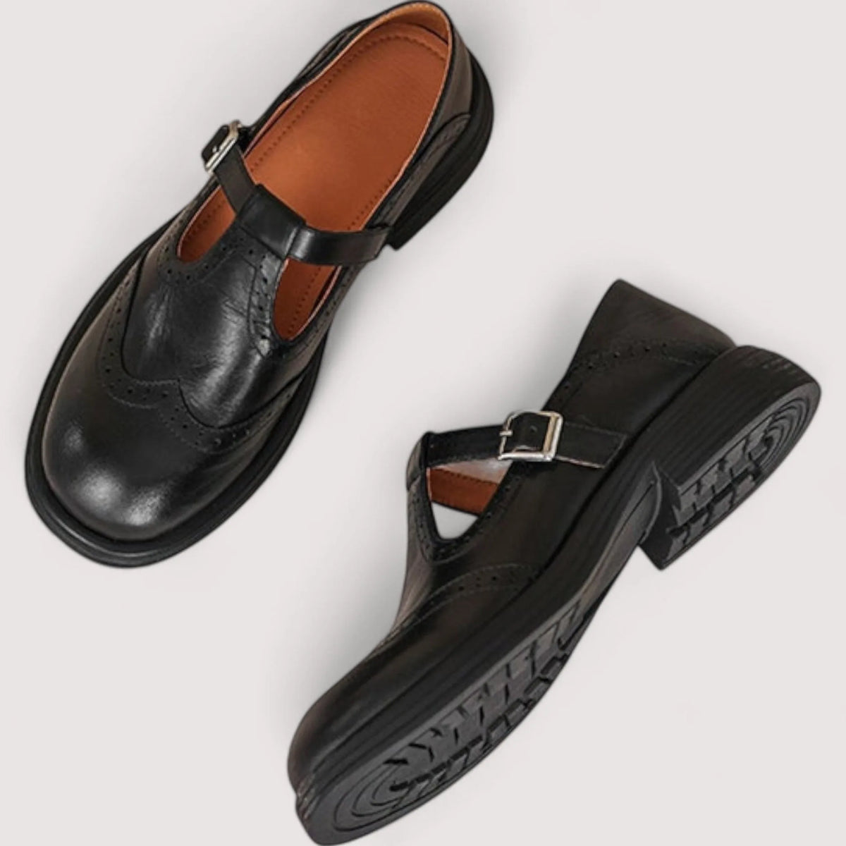 Overhead view of black leather Mary Janes showing tan interior lining, buckle strap and brogue wingtip toe