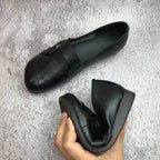 Black leather flat paired with the sole turned up, held in hand to display the wedge heel height