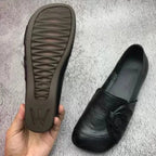 Textured rubber sole with brand logo held beside a black leather flat with knotted toe detail