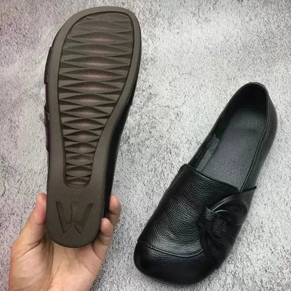 Textured rubber sole with brand logo held beside a black leather flat with knotted toe detail